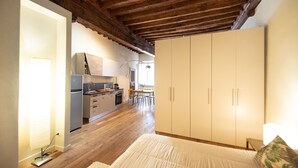 A bedroom with a wooden ceiling, a bed, a wardrobe, and a kitchen in the background. - Dante´s Home Cozy in Center Town (Lucca)