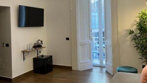 A modern living room with a flat-screen TV, a small shelf with items, a black cabinet, and a wooden floor. - Residenza Toledo (Naples)