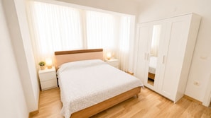 Een slaapkamer met een bed, nachtkastjes, een kledingkast en een raam met gordijnen.