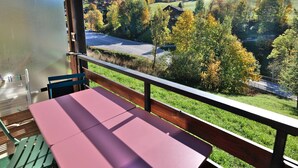 A balcony with a table and chairs, overlooking a valley with trees and a road.