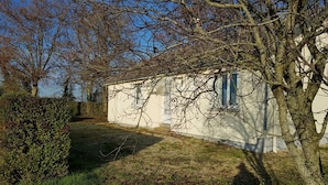 A white building with a small porch and a tree in front.
