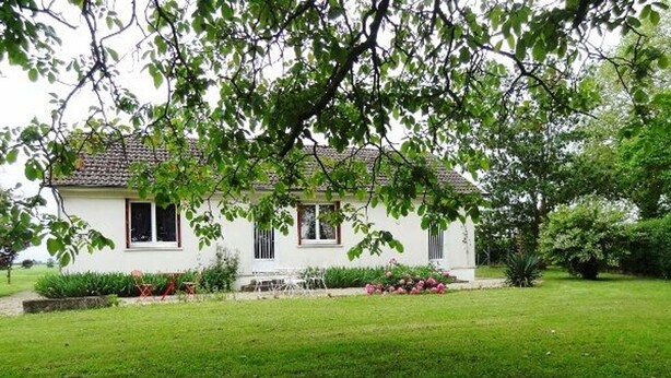 A white house with a tiled roof, surrounded by a well-maintained lawn and flowering plants.