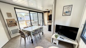 Una sala de estar moderna con comedor, ventanas amplias, un televisor de pantalla plana y una pequeña mesa con una planta.