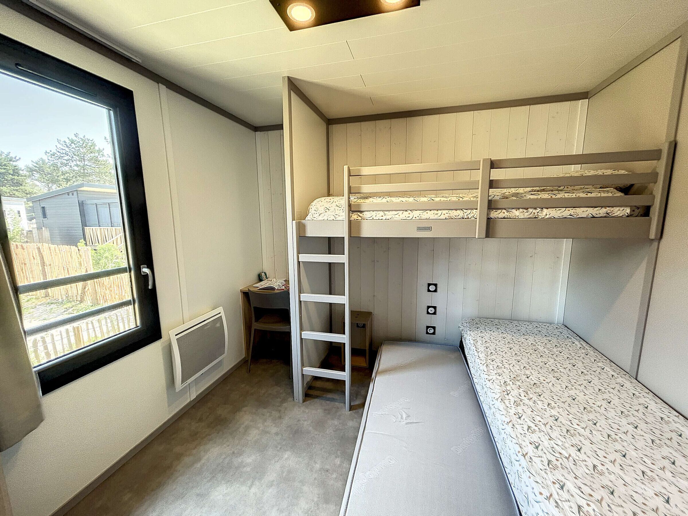 Ein kleines Zimmer mit Etagenbetten, einem Schreibtisch und einem Fenster mit Blick auf einen eingezäunten Bereich.
