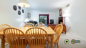 Un comedor con una mesa y sillas de madera, una lámpara colgante y un televisor al fondo.