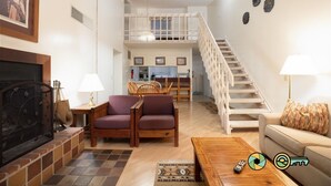 A spacious living room with a fireplace, a dining area, and a staircase leading to an upper level. - Mountainside Retreat Condo (#1-302) | Top-level w/ loft | Quiet & secluded (Basye)