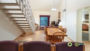 A staircase leading to a second floor, a dining area with a wooden table and chairs, and a television in the background. - Mountainside Retreat Condo (#1-302) | Top-level w/ loft | Quiet & secluded (Basye)