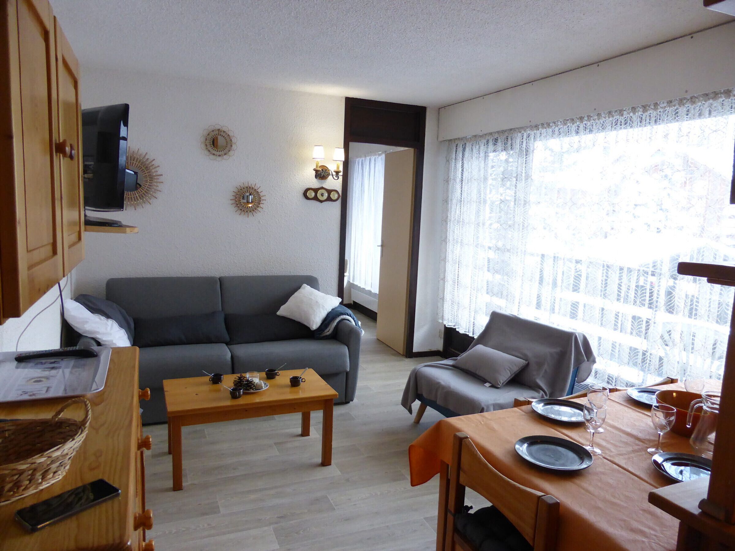 A living room with a sofa, a dining table set for two, and a television mounted on the wall.
