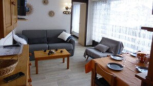 A living room with a sofa, a dining table set for two, and a television mounted on the wall.
