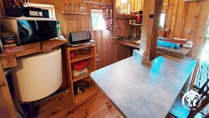 Interior de madera con una zona de cocina que incluye un microondas, un refrigerador pequeño, una computadora portátil y diversos utensilios de cocina.