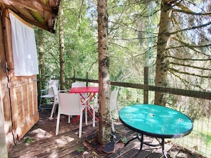 Una terraza de madera con mesa y sillas, rodeada de árboles.