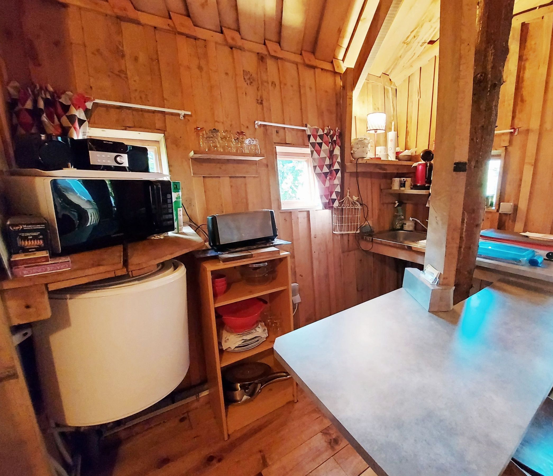 Un intérieur en bois comprenant un coin cuisine équipé d’un four à micro-ondes, d’un petit réfrigérateur, d’un ordinateur portable et de divers ustensiles de cuisine.
