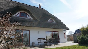 A house with a thatched roof, two windows with red frames, and a bench outside.