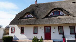 Une maison traditionnelle avec un toit de chaume, des murs blancs et des fenêtres à cadre rouge.