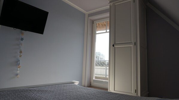 A bedroom with a bed, a television mounted on the wall, and a window with a view of a fence and trees.