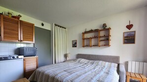 A bedroom with a bed, a wooden table, a TV, a shelf with decorative items, and a chair. - Cozy studio in village center, pets allowed, private parking (Samoëns)