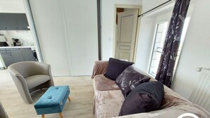 A modern living room with a sofa, a chair, and a small ottoman. There is a kitchen area visible in the background. - Charming Renovated Stone House on a Farm with Modern Amenities, Near Scenic Trails (Champéon)