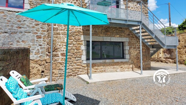 A stone building with a balcony and a staircase. There is a turquoise umbrella and white lounge chairs with blue cushions. - Charming Renovated Stone House on a Farm with Modern Amenities, Near Scenic Trails (Champéon)