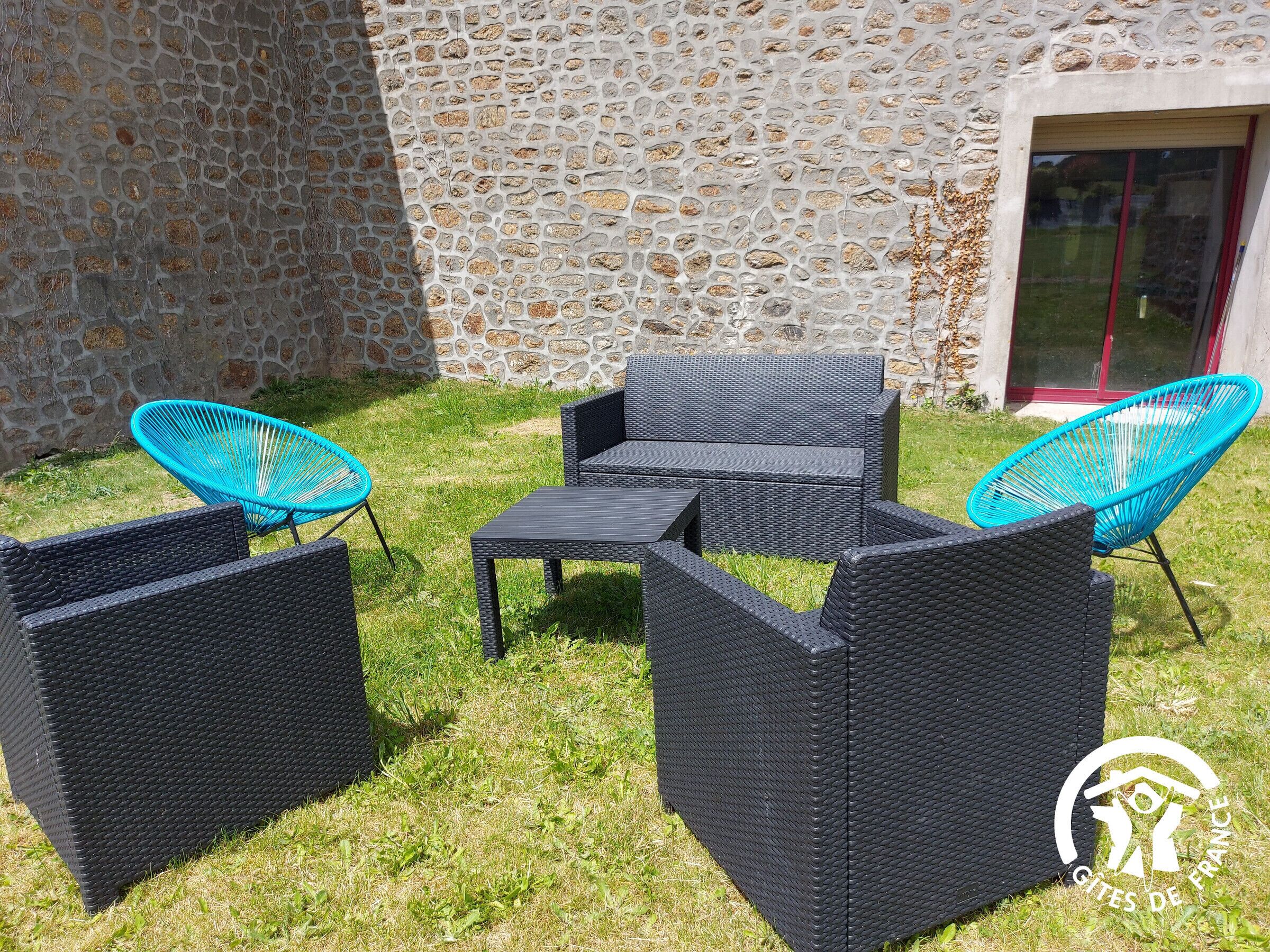 An outdoor seating area with wicker furniture and chairs, set against a stone wall and a glass door.