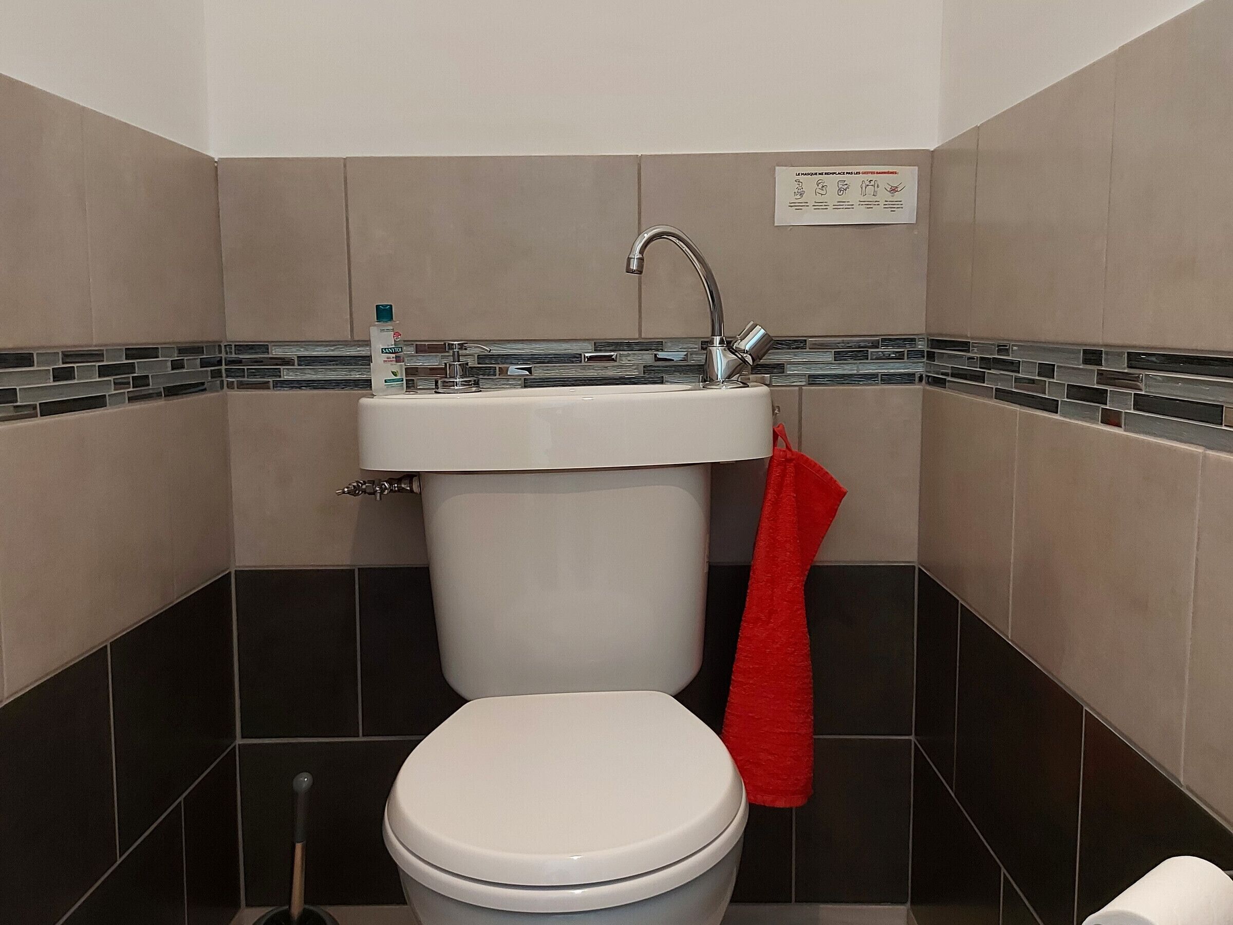 A bathroom with a white toilet, a sink with a faucet, and a red towel hanging on the wall.