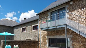 A stone building with a balcony and a gravel patio with lounge chairs. - Charming Renovated Stone House on a Farm with Modern Amenities, Near Scenic Trails (Champéon)