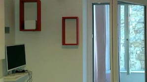 Quarto com televisão sobre suporte, porta com vista para uma parede de pedra e dois quadros com moldura vermelha na parede.