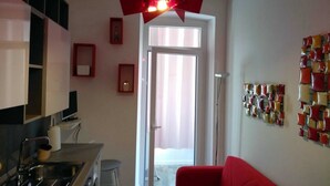 Uma cozinha compacta com uma luminária pendente vermelha moderna, uma área de refeições com uma cadeira vermelha e uma parede com uma obra de arte abstrata colorida.