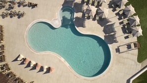 Vista aérea de una piscina con forma singular, rodeada de sillas de descanso y sombrillas.