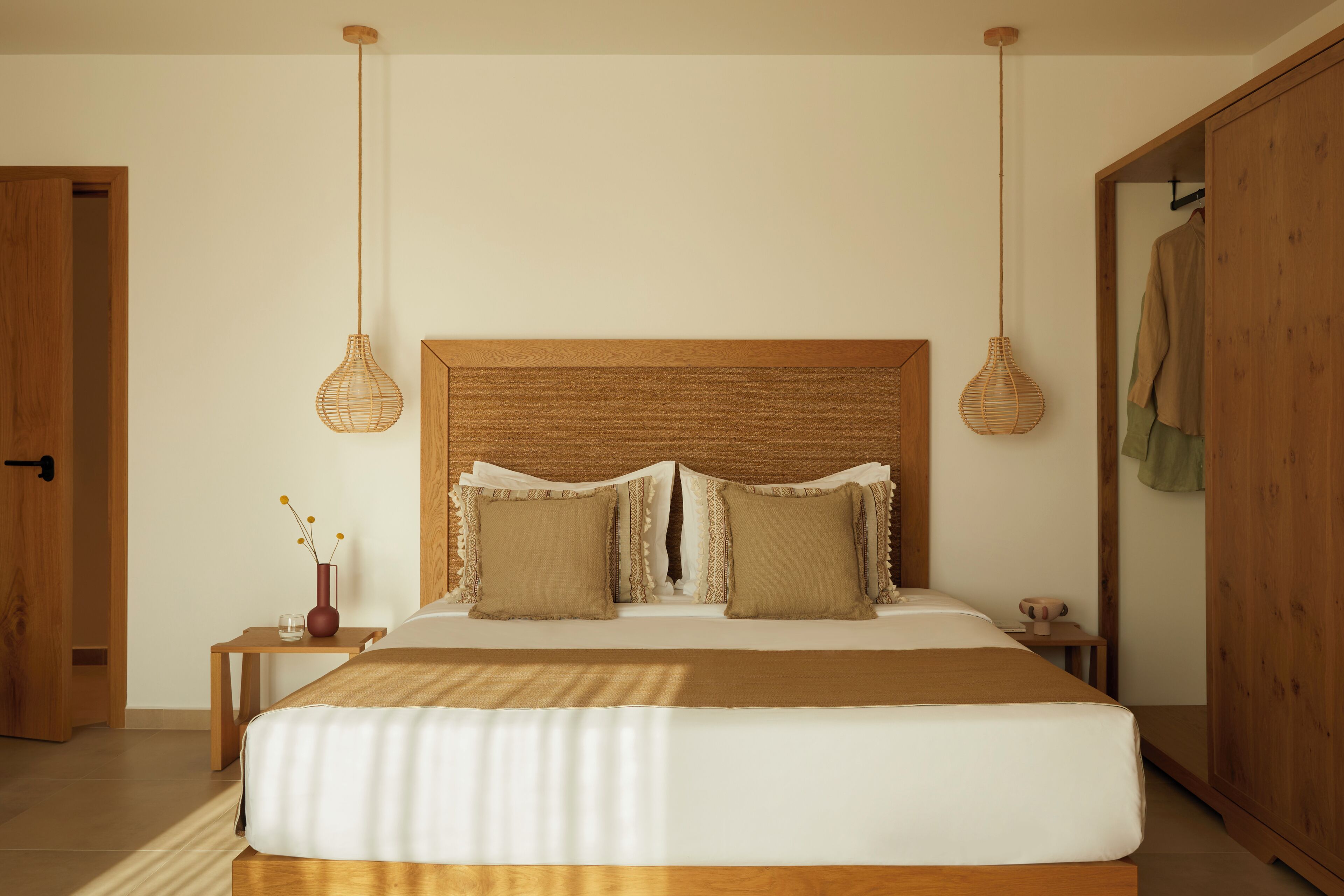 A bedroom with a large bed, wooden headboard, two bedside tables, and hanging wicker lamps.