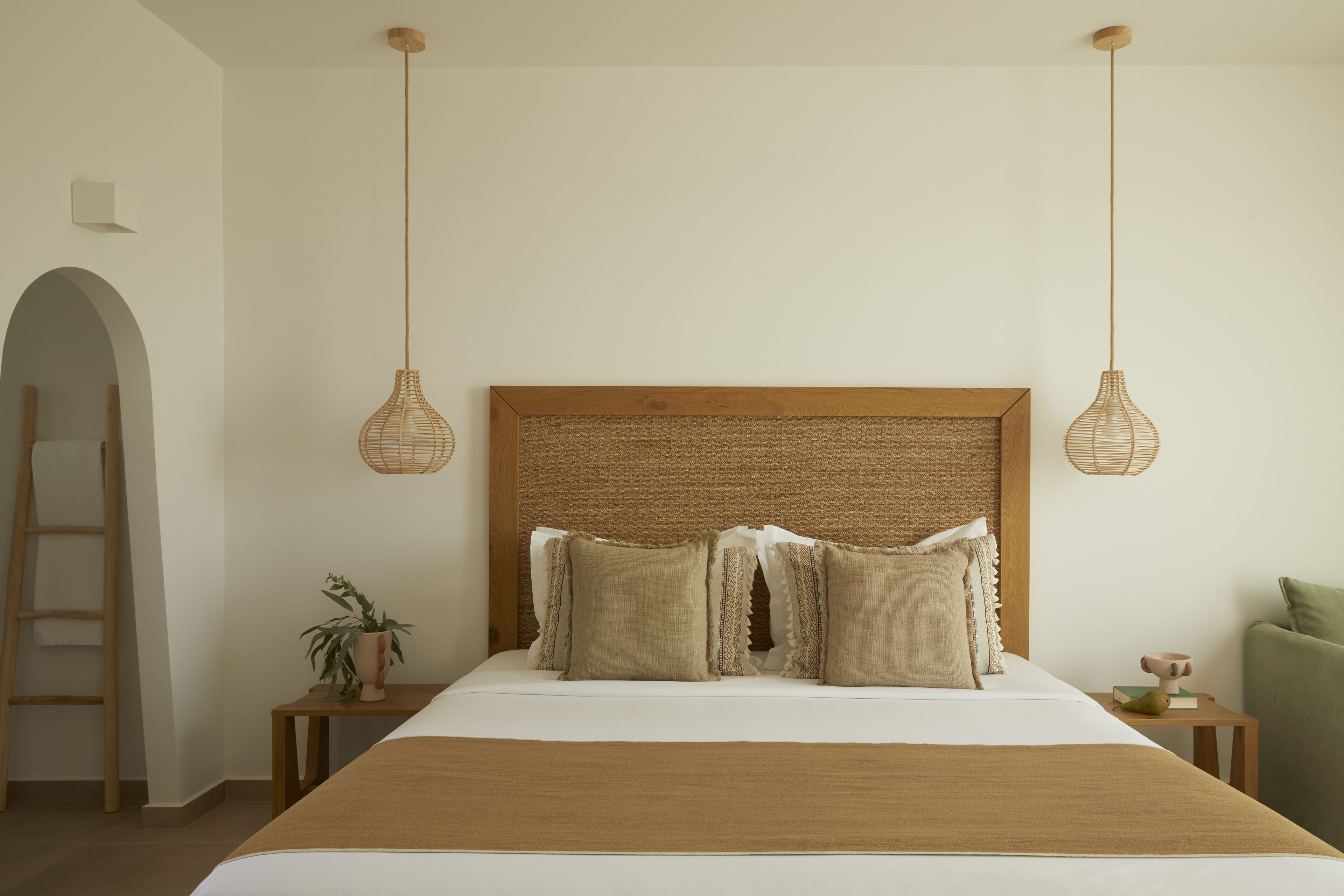 A neatly arranged bedroom with a large bed, two bedside tables, a ladder, and a hanging light fixture.