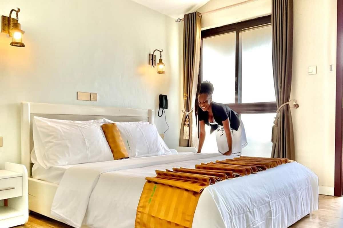 A hotel room with a neatly made bed, a bedside table, and a large window with curtains.