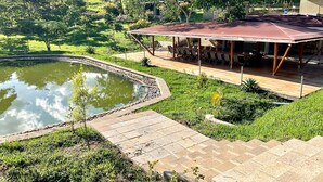 A serene outdoor area with a pond, a wooden deck, and a covered seating area. - Zebi Ecolodge (Hoima)