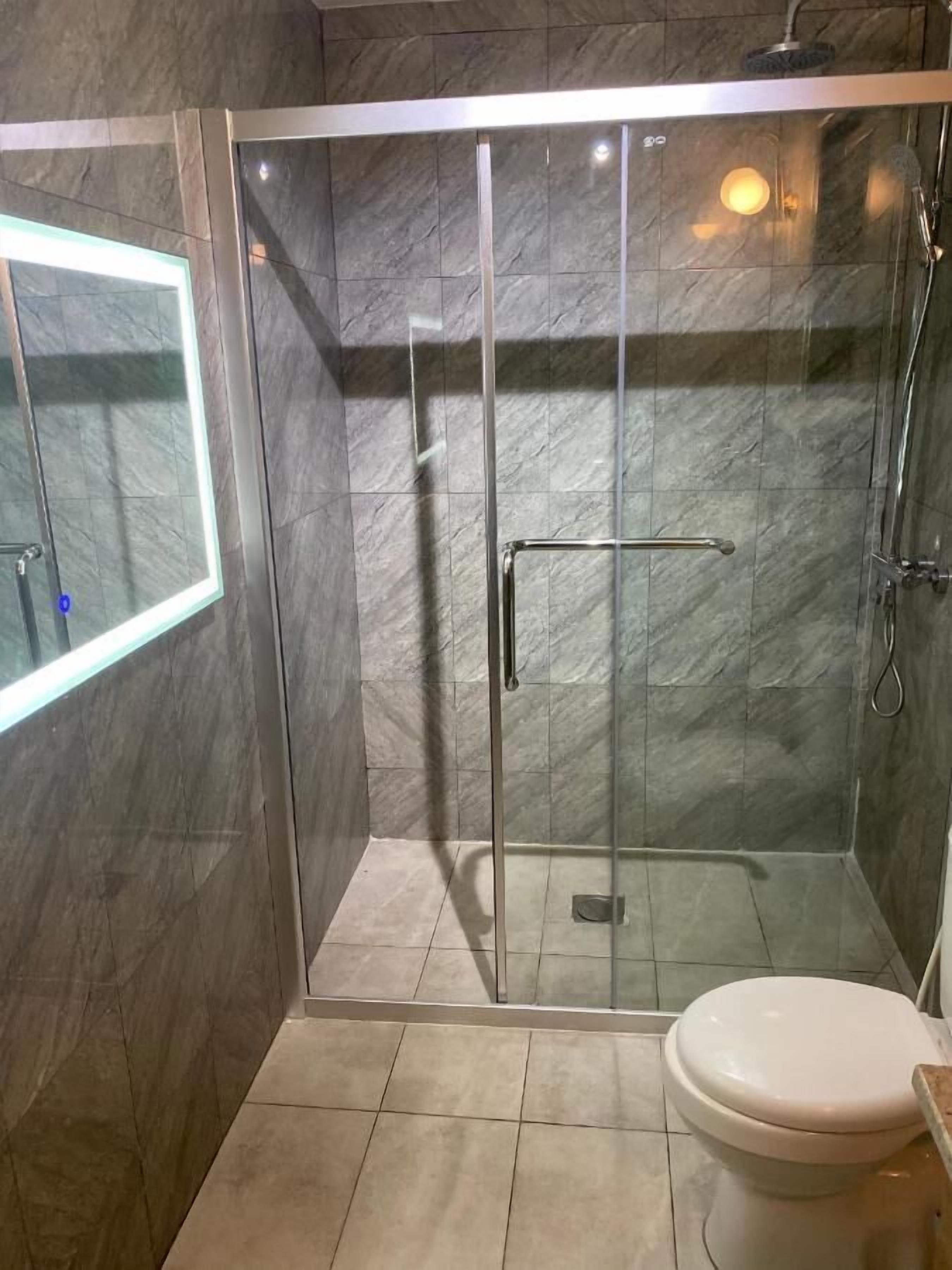 Een moderne badkamer met een glazen douchecabine, een toilet en een spiegel.