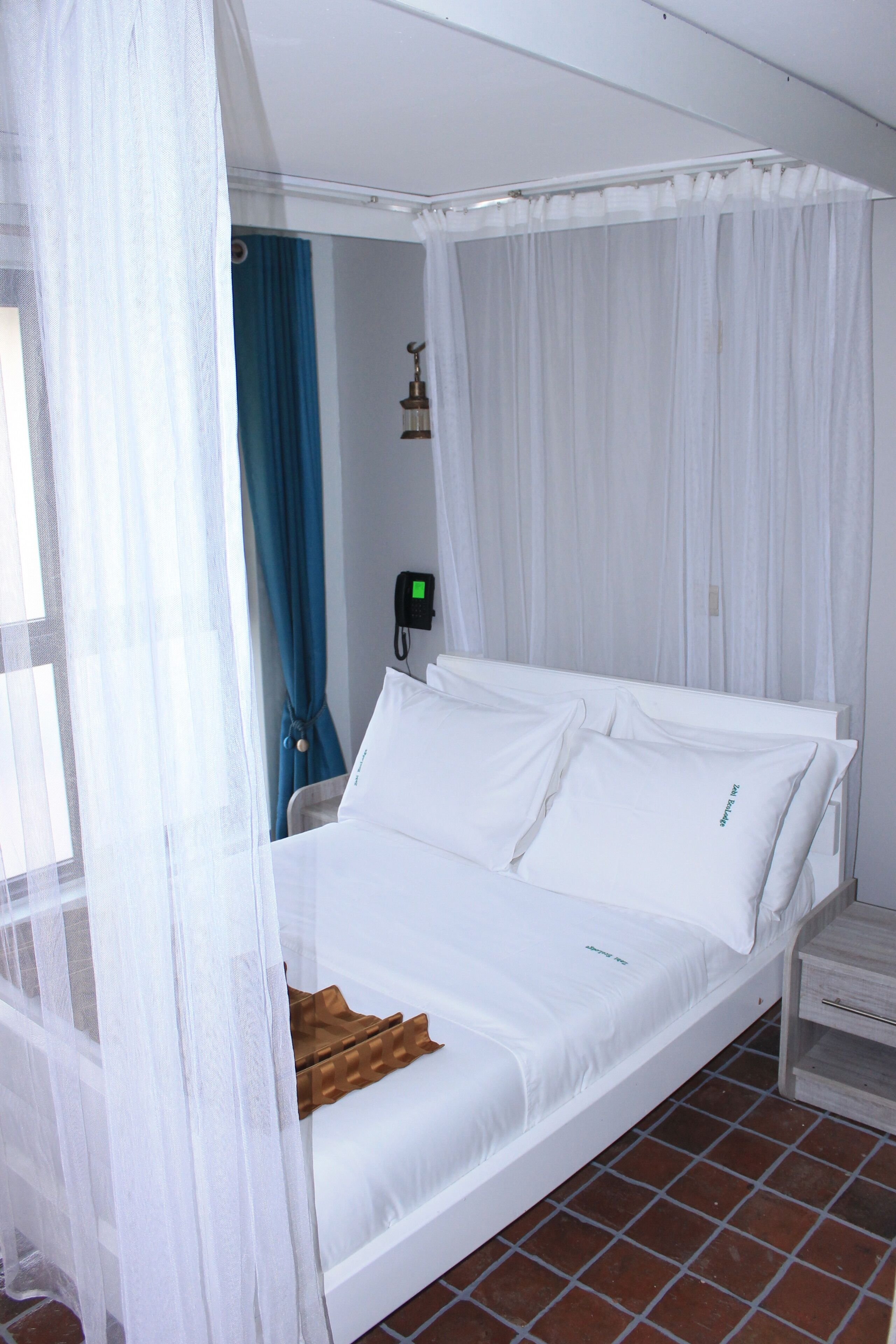 A single bed with white bedding, a bedside table, and a curtain.