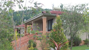 A house with a red roof, a staircase leading to a porch, and a garden with various plants. - Zebi Ecolodge (Hoima)