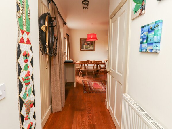 A hallway with wooden flooring, a dining area with a red lamp, and a wall with a framed picture. - Harness Lodge (Seahouses)