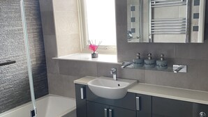 Uma casa de banho moderna com uma banheira, uma pia e uma sanita. Há uma janela sobre a pia e um espelho sobre a sanita.