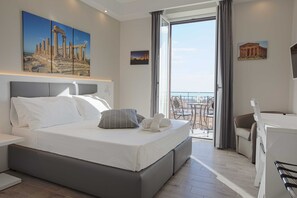 A modern hotel room with a large bed, a desk, and a balcony with a view of the city. - Esseneto Rooms (Agrigento)