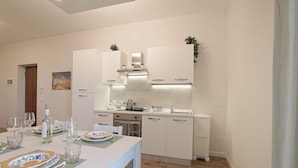 A modern kitchen with white cabinetry, a dining table set with plates and glasses, and a small island with a sink. - Esseneto Rooms (Agrigento)