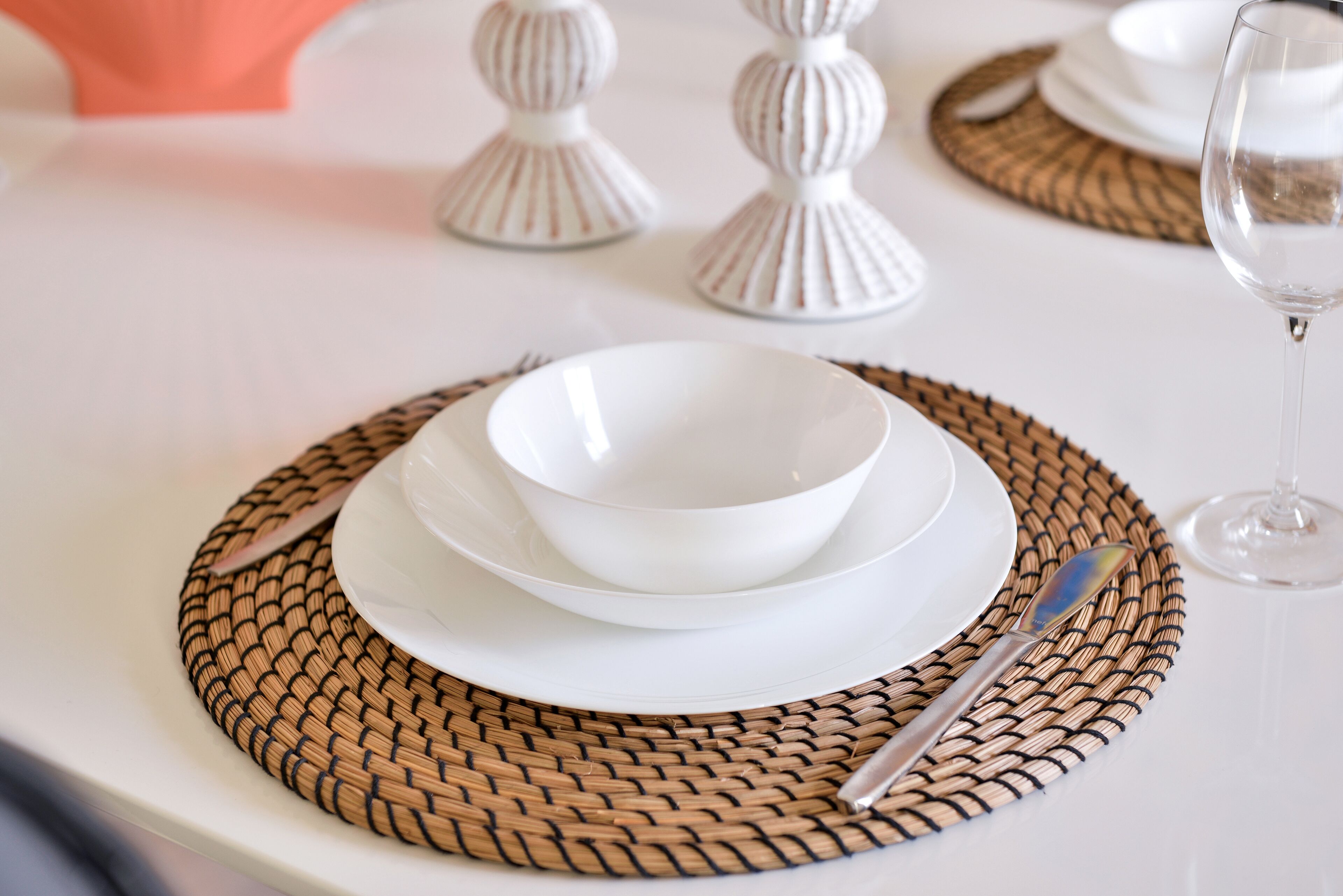 A table set with white plates, bowls, and a knife on a woven placemat.