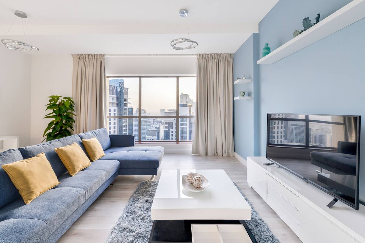 A modern living room with a blue sofa, a white coffee table, and a large TV on a white stand.