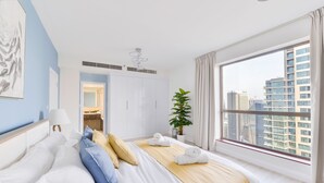 Una habitación de hotel moderna con una cama grande, una planta en maceta y vistas de la ciudad a través de un amplio ventanal.