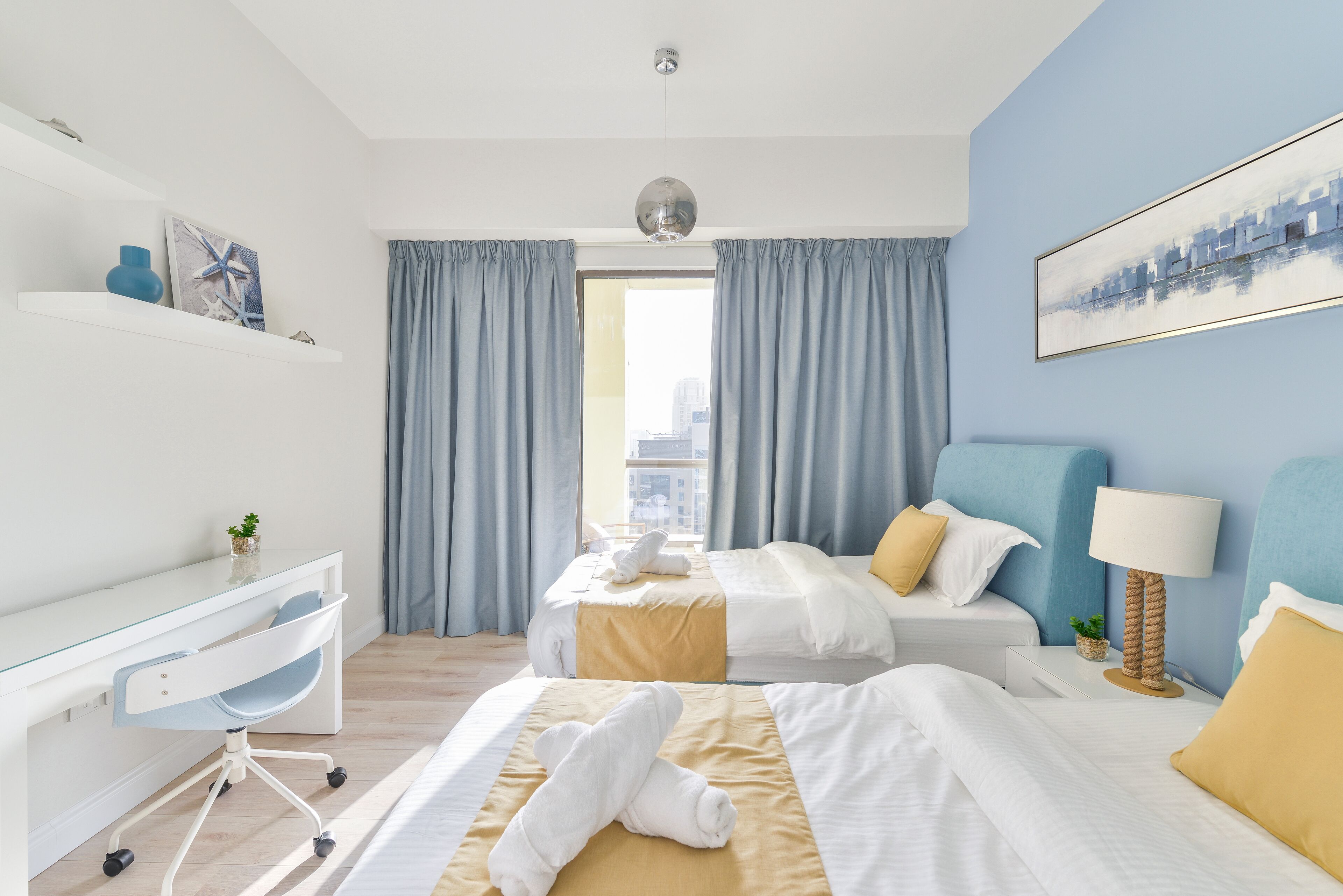 Hotellihuone, jossa on työpöytä, kaksi sänkyä, näköala kaupunkiin ja moderni kattokruunu.