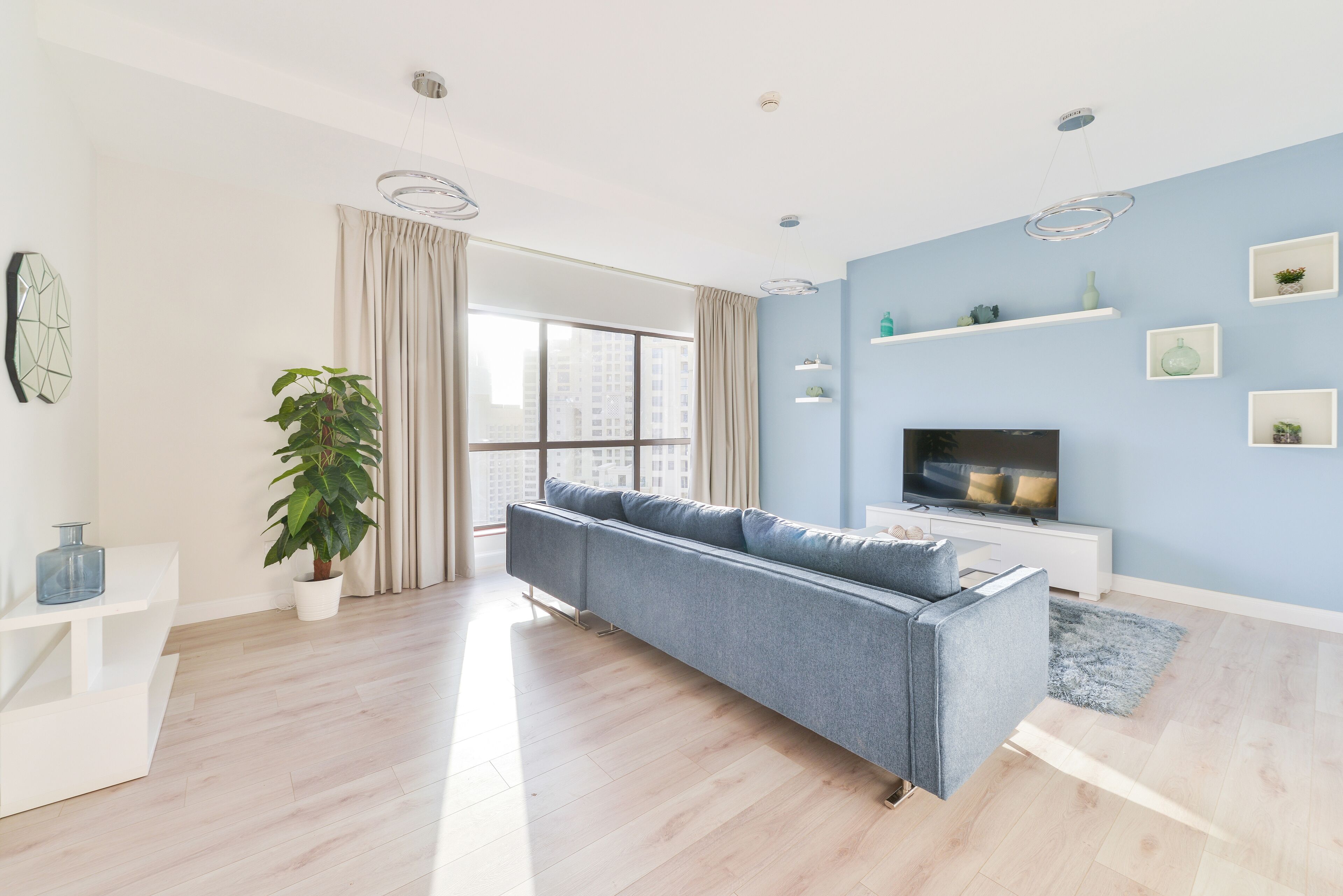 A modern living room with a grey sofa, a TV, and a large window with curtains.