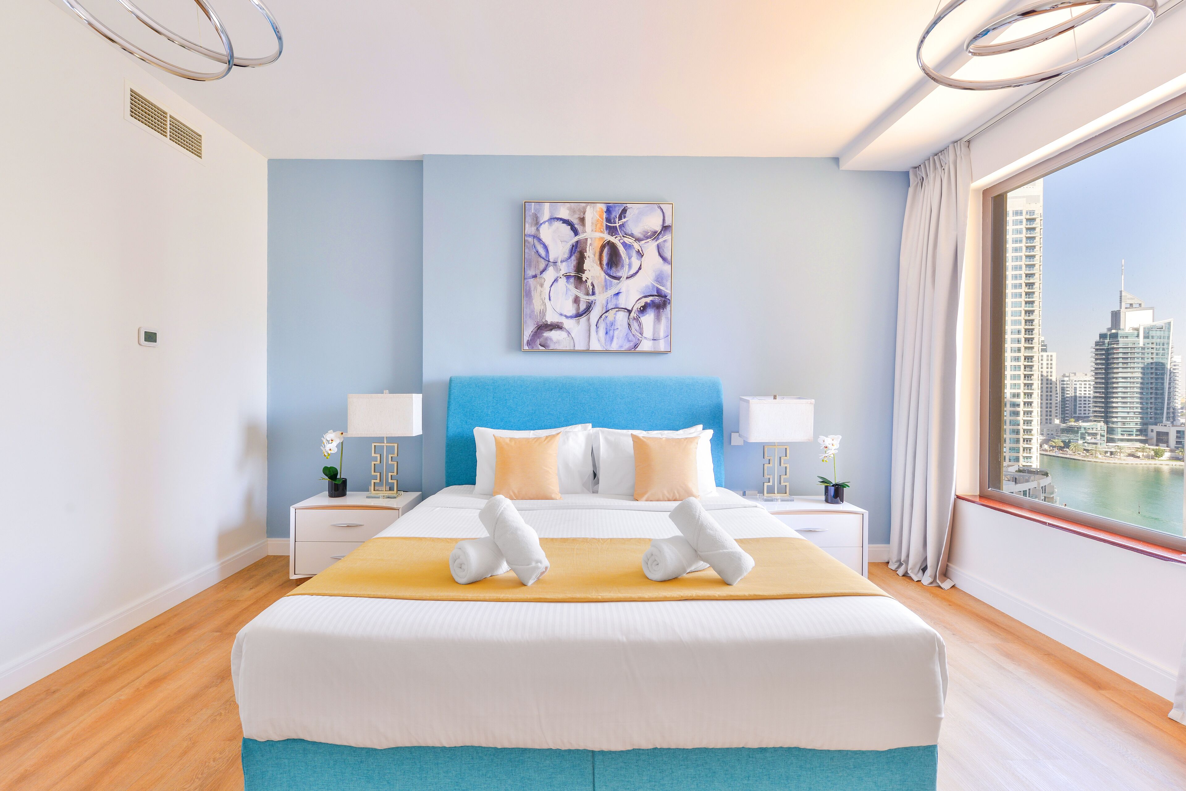 Une chambre d’hôtel moderne avec un grand lit, une vue sur la ville et un mur d’accent bleu.