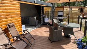 A wooden cabin with a patio area featuring wicker furniture, a table with drinks, and a grill. - Rowan Boutique Lodge for Couples With a dog (York)