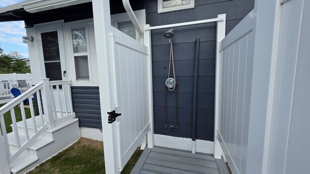 A two-story house with a dark grey exterior and white trim. There is a front door with a small window above it, and a set of stairs leading to the front porch. - Coastal Cottage~Fenced Yard~Fire Pit~Pet Friendly! (Villas)