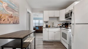 A modern kitchen with white cabinets, a built-in oven, and a microwave. There is a wooden dining table with benches. - Coastal Cottage~Fenced Yard~Fire Pit~Pet Friendly! (Villas)