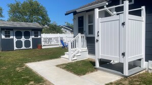 A residential property with a white garage door, a concrete pathway, and a small porch with steps. - Coastal Cottage~Fenced Yard~Fire Pit~Pet Friendly! (Villas)