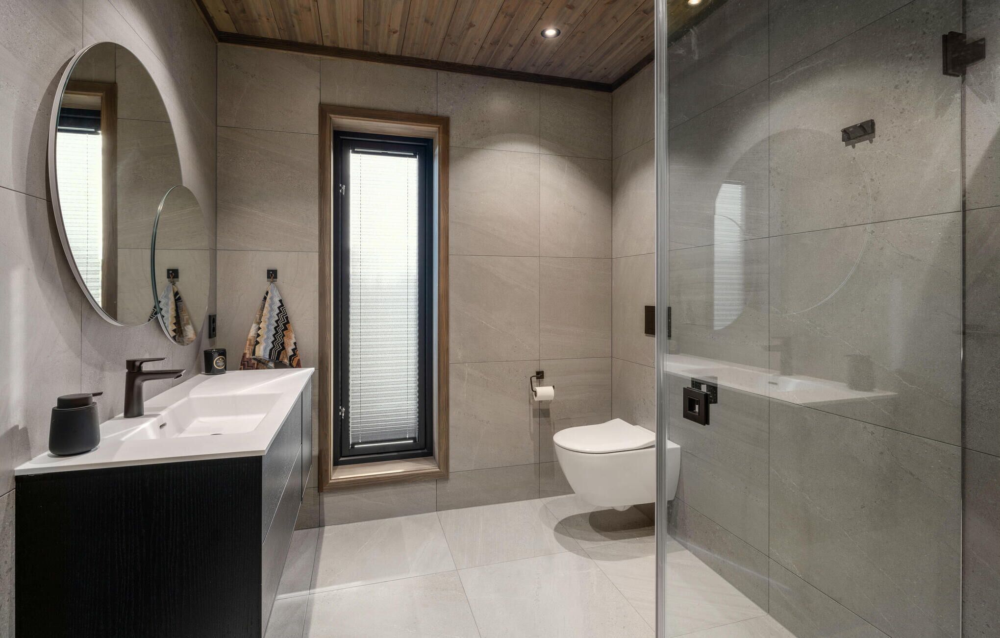 Un baño moderno con un espejo grande, un lavamanos, un inodoro y una zona de ducha.